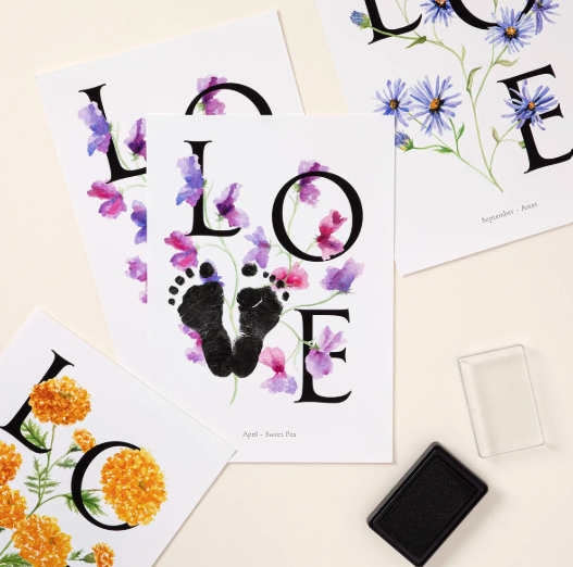 Three prints of the word LOVE illustrated with watercolor birth-month flowers, the center one with a baby's inked footprints forming the O, beside a black ink pad