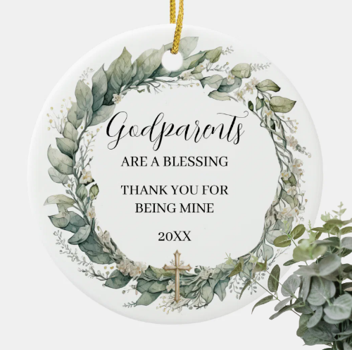 Round white ceramic ornament with a eucalyptus and white flower wreath around the words Godparents are a blessing, thank you for being mine, and the year