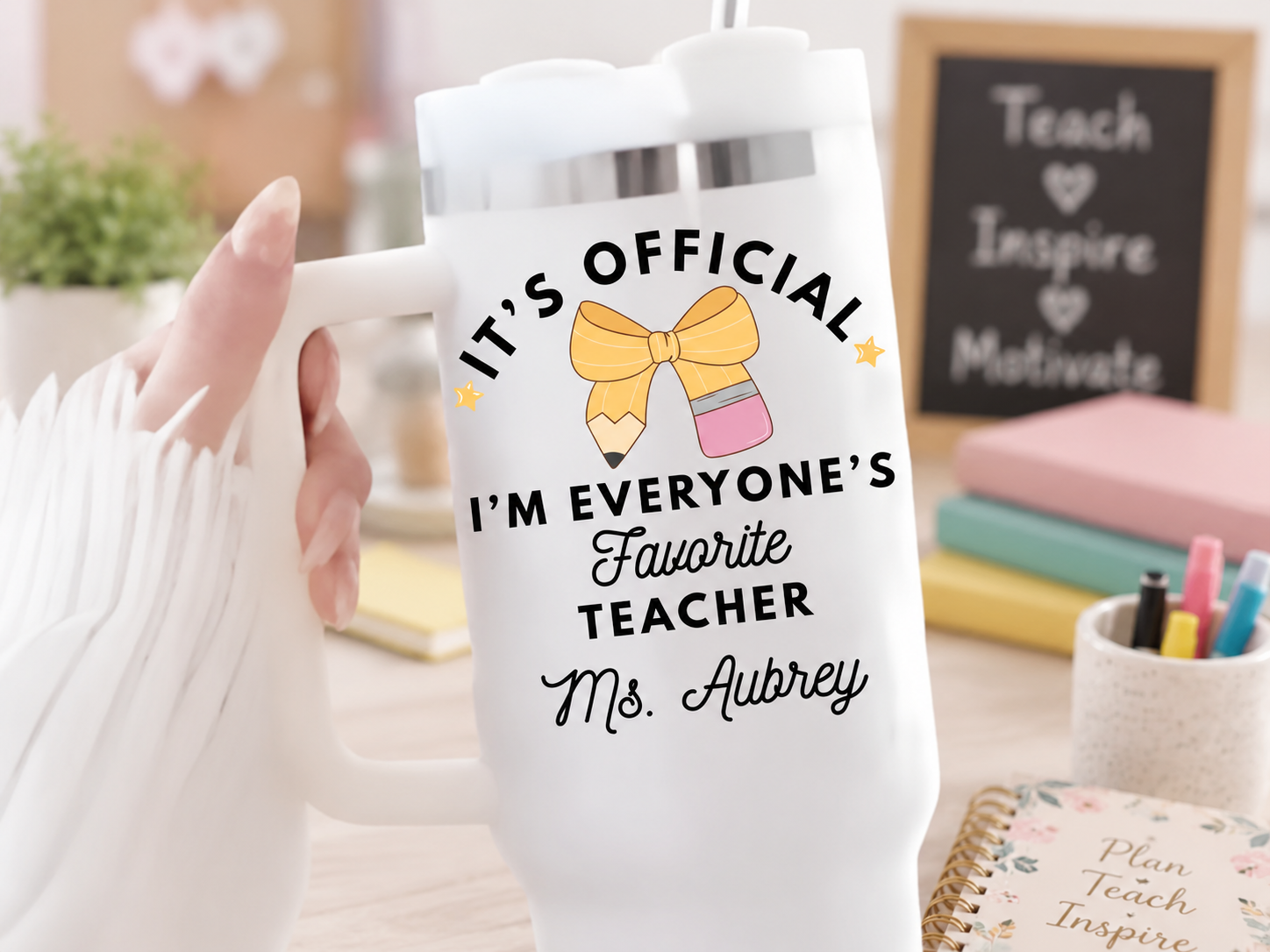 White personalized 40 oz teacher tumbler with 'It's Official I'm Everyone's Favorite Teacher Ms. Aubrey' design featuring a yellow pencil-and-bow illustration