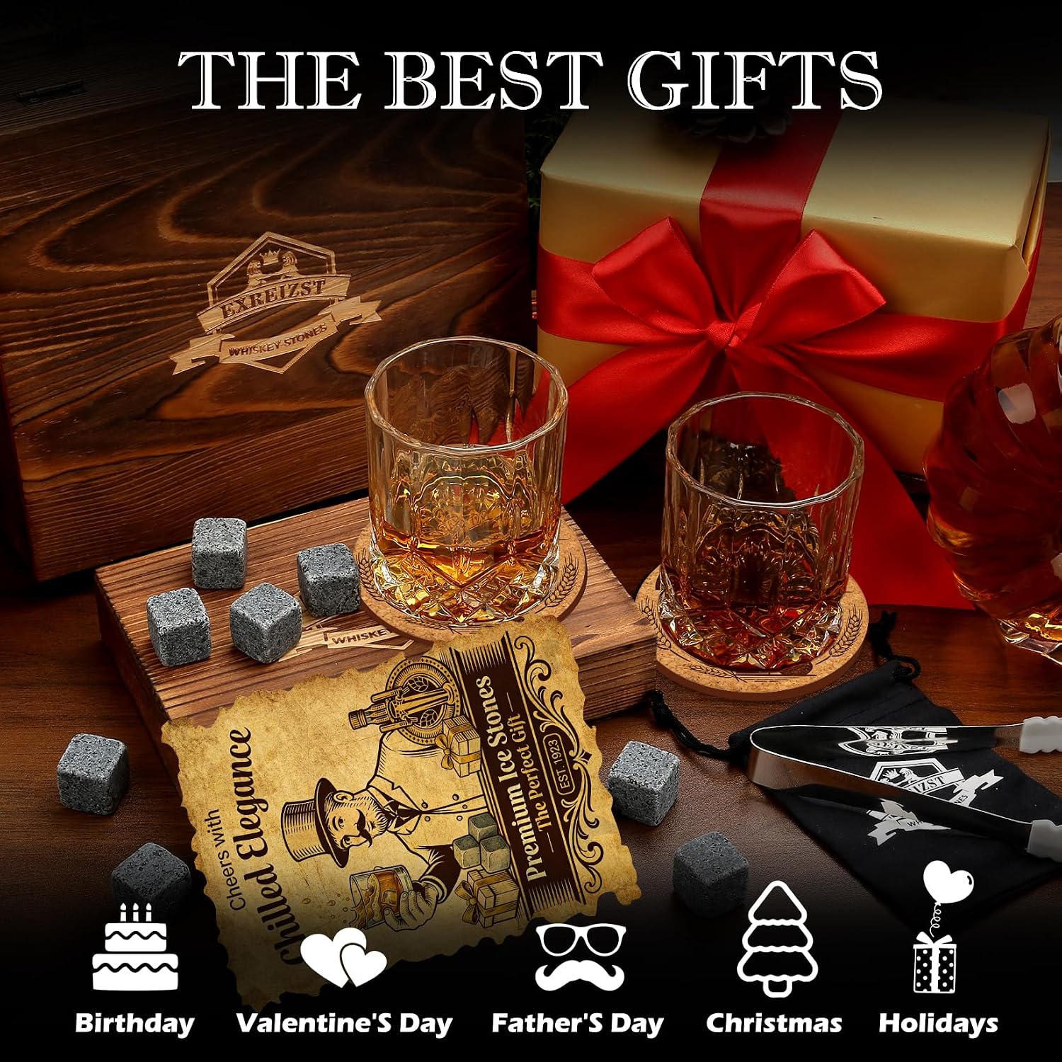 Two cut-glass whiskey tumblers with wooden coasters, granite chilling stones and tongs beside an engraved wooden gift box