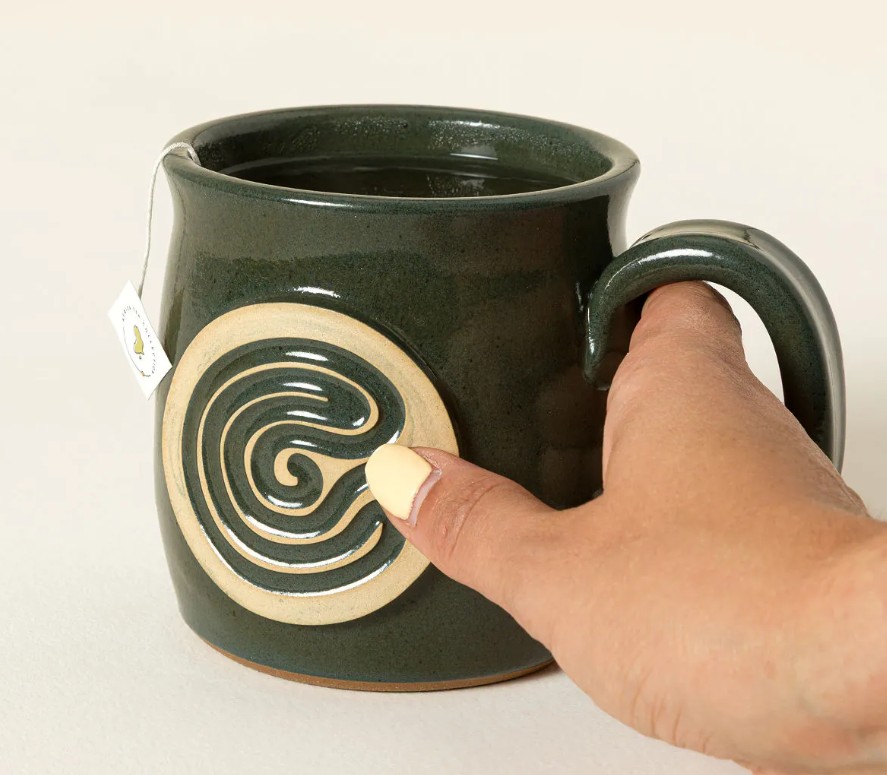 Deep green artisan stoneware finger tracing meditation mug for daycare teachers with a raised spiral labyrinth design being traced with a thumb