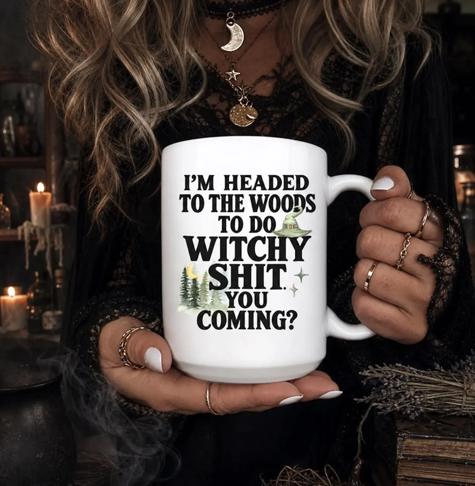 White ceramic mug printed with I'm headed to the woods to do witchy shit, you coming, with a witch hat, pines, and a crescent moon