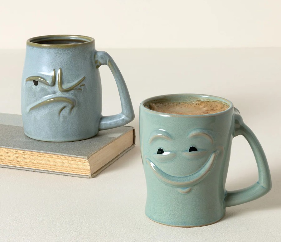 Artisan sculpted stoneware Morning Mood coffee mug gift for husband with grumpy and happy face designs in soft blue reactive glaze on a book