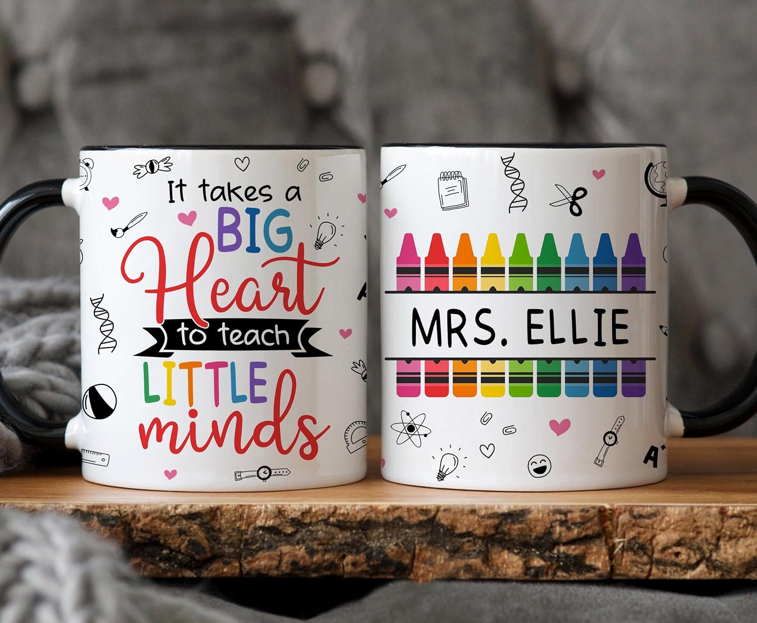 Two black-handled ceramic daycare teacher gift mugs, one with colorful 'It Takes a Big Heart to Teach Little Minds' lettering and the other with a rainbow crayon design and personalized 'Mrs. Ellie' name, displayed on a wooden slice