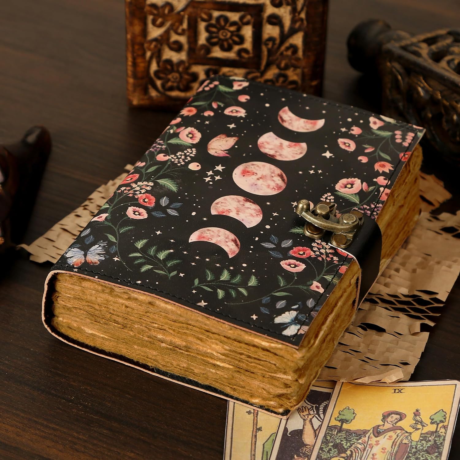 Black journal with blush pink moon phases and floral vines across the cover, a brass swing clasp, and thick deckle-edged pages
