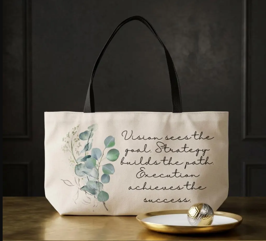 Cream canvas tote bag with black handles, a watercolor eucalyptus print and script text reading Vision sees the goal. Strategy builds the path. Execution achieves the success.