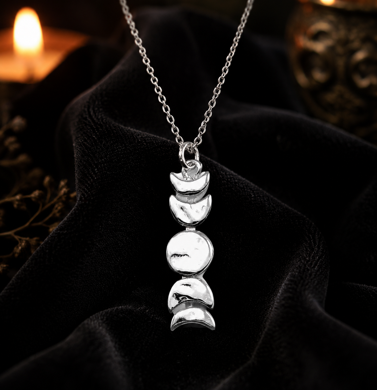Sterling silver moon phase pendant necklace with five lunar phases from crescent to full, displayed on black velvet by candlelight