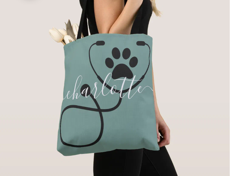 Sage green canvas tote bag printed with a black stethoscope forming a paw print and the name Charlotte in white script