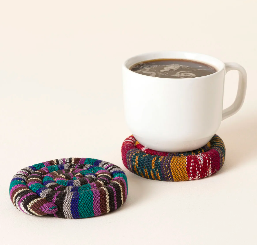 Two woven striped fabric warming coasters in jewel tones, one holding a white mug of coffee