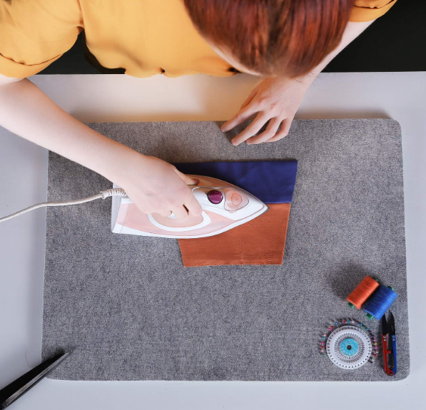 Person pressing fabric with an iron on a large gray wool quilting pad